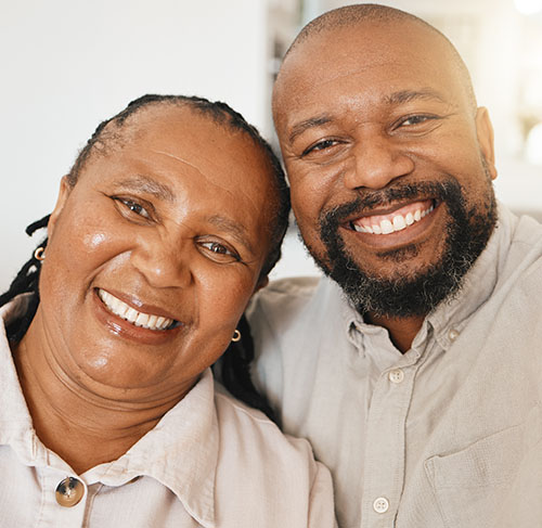 Elderly woman hugging her significant other over the shoulders and smiling at the camera.