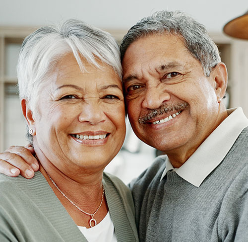 Elderly woman hugging her significant other over the shoulders and smiling at the camera.
