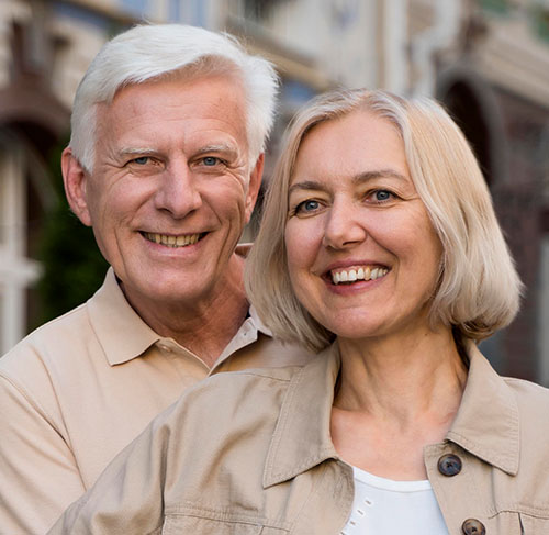 Elderly woman hugging her significant other over the shoulders and smiling at the camera.