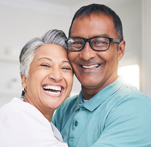 Elderly woman hugging her significant other over the shoulders and smiling at the camera.