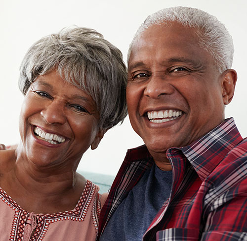 Elderly woman hugging her significant other over the shoulders and smiling at the camera.