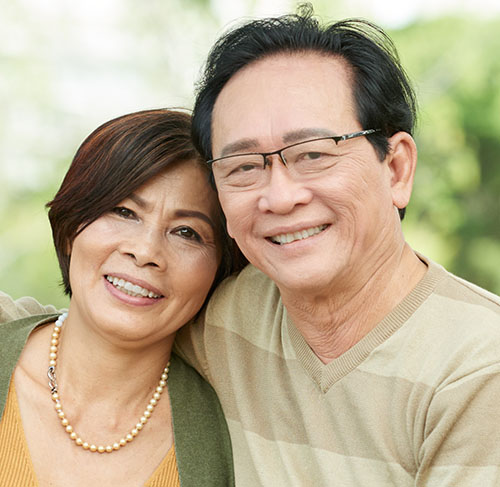 Elderly woman hugging her significant other over the shoulders and smiling at the camera.