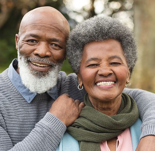 Elderly woman hugging her significant other over the shoulders and smiling at the camera.