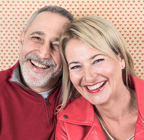 Elderly woman hugging her significant other over the shoulders and smiling at the camera.
