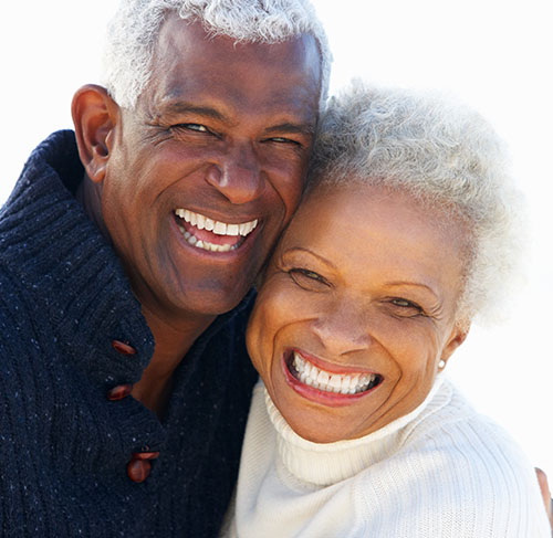Elderly woman hugging her significant other over the shoulders and smiling at the camera.