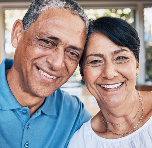 Elderly woman hugging her significant other over the shoulders and smiling at the camera.
