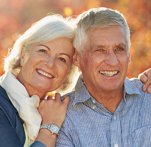 Elderly woman hugging her significant other over the shoulders and smiling at the camera.