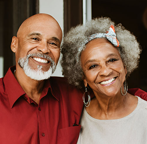 Elderly woman hugging her significant other over the shoulders and smiling at the camera.