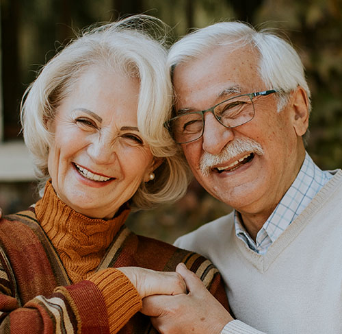 Elderly woman hugging her significant other over the shoulders and smiling at the camera.