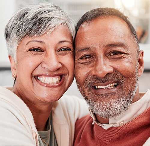 Elderly woman hugging her significant other over the shoulders and smiling at the camera.