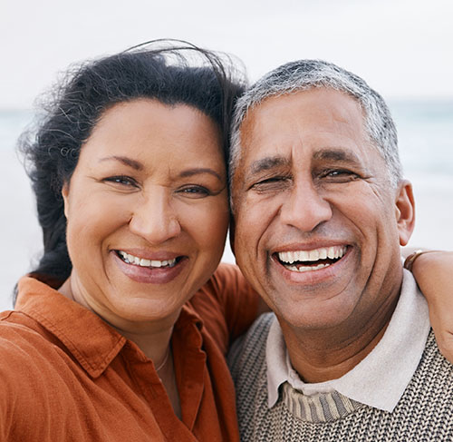 Elderly woman hugging her significant other over the shoulders and smiling at the camera.
