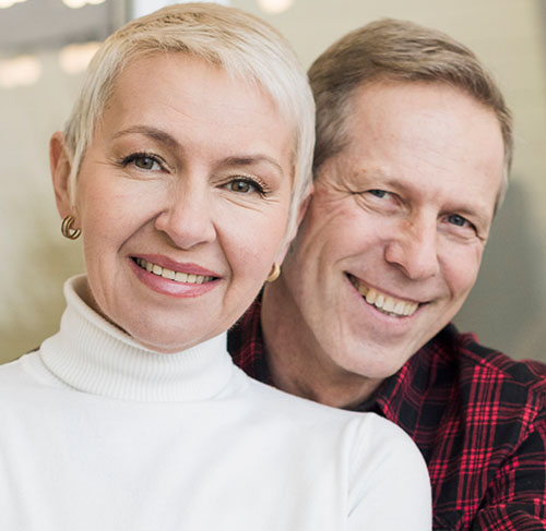 Elderly woman hugging her significant other over the shoulders and smiling at the camera.