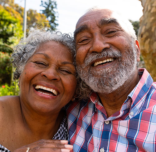 Elderly woman hugging her significant other over the shoulders and smiling at the camera.