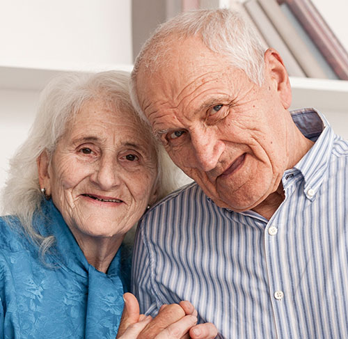 Elderly woman hugging her significant other over the shoulders and smiling at the camera.