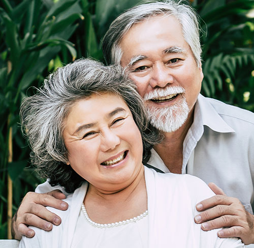 Elderly woman hugging her significant other over the shoulders and smiling at the camera.