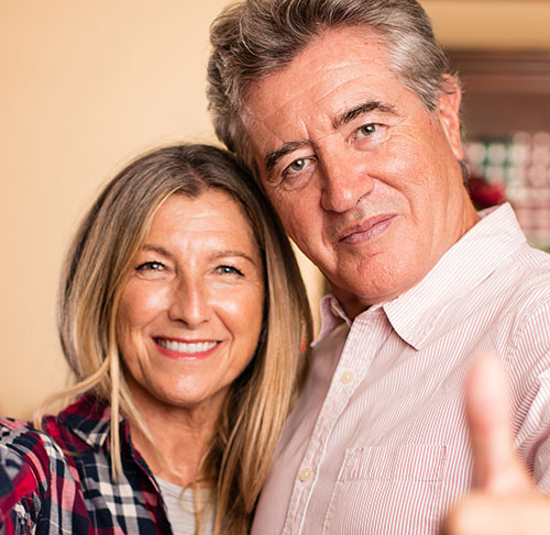 Elderly woman hugging her significant other over the shoulders and smiling at the camera.