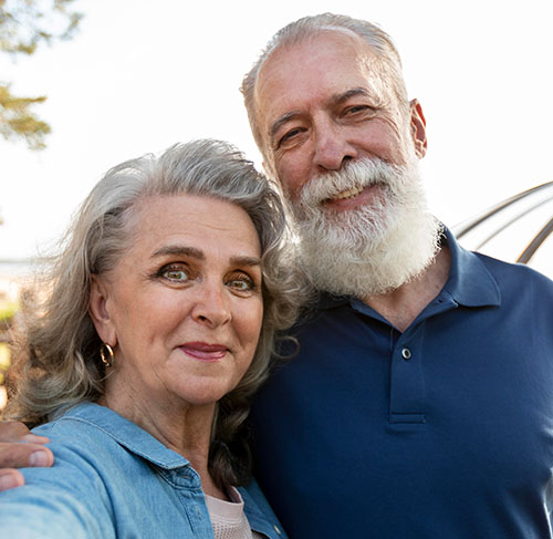 Elderly woman hugging her significant other over the shoulders and smiling at the camera.