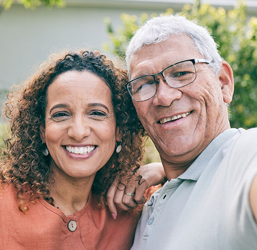 Elderly woman hugging her significant other over the shoulders and smiling at the camera.